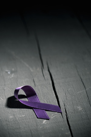 a purple ribbon for the awareness about the unacceptability of the violence against women, on a dark gray rustic wooden surfaceの写真素材