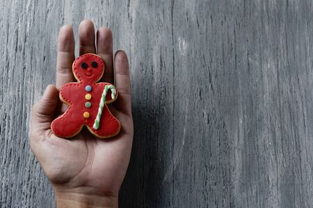 closeup of the hand of a young cacausian man with a homemade cookie in the shape of a gingerbread man on a gray rustic wooden surface, with a blank space on the rightの写真素材