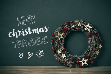 a nice christmas wreath with red fruits and golden stars, and the text merry christmas teacher in a green chalkboardの写真素材