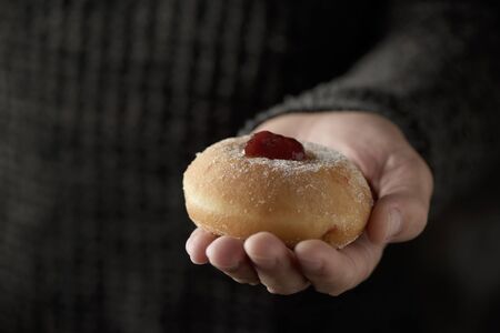 closeup of a sufganiyah, a Jewish donut filled with strawberry jelly traditionally eaten on Hanukkah, in the hand of a manの写真素材