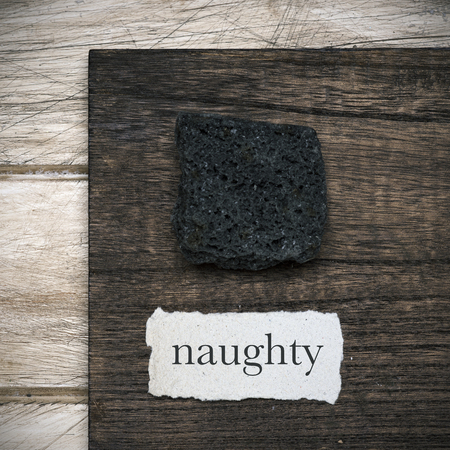 high angle view of a piece of candy coal next to a piece of paper with the word naughty written in it, on a rustic wooden tableの写真素材