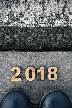 high angle view of four wooden numbers forming the number 2017 as the new year, and the feet of a man wearing blue shoes stepping on the asphaltの写真素材