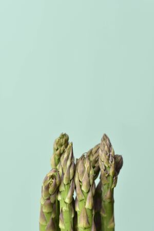 closeup of a bunch of raw garden asparagus on a pale green background with some blank space on topの写真素材