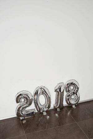 some silvery number-shaped balloons forming the number 2018, as the new year, on a tiled floor, against a white background with a blank space on topの写真素材
