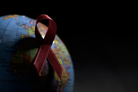 closeup a world globe with a red ribbon for the fight against AIDS on a black background with a blank space on the rightの写真素材