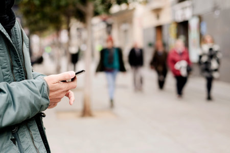closeup of a young caucasian man wearing a green parka using a smartphone in the street