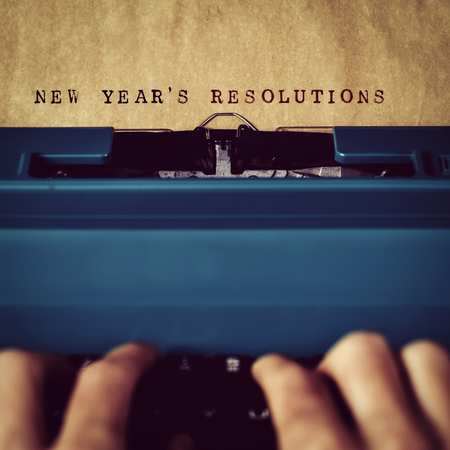 closeup of a man typewriting the text new years resolutions in a yellowish paper with a blue retro typewriterの写真素材