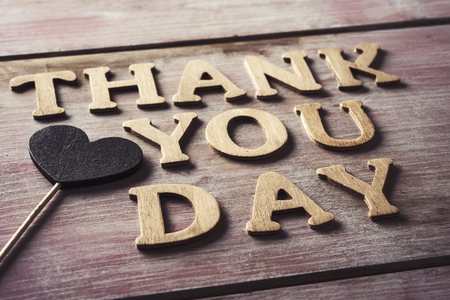 some wooden letters forming the text thank you day and a heart attached to a stick on a rustic wooden surfaceの写真素材
