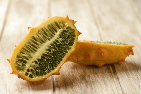 closeup of a kiwano or horned melon cut in halves on a white rustic wooden tableの写真素材