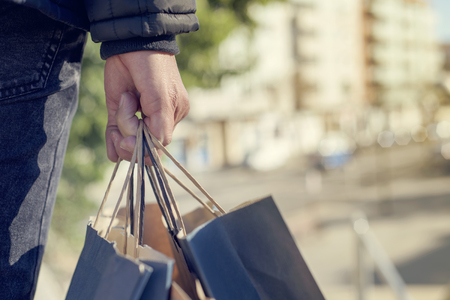 closeup of a young caucasian man seen from behind carrying some paper shopping bags with his purchases on the streetの写真素材