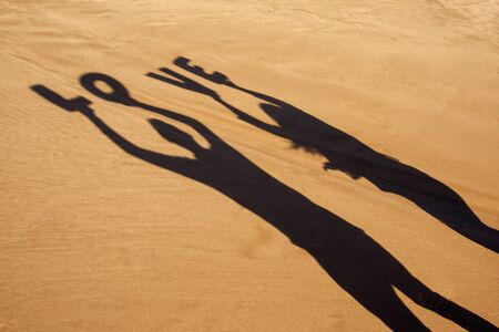 closeup of the shadow of a man and a woman holding some letters forming the word love over their heads on the sand of a beachの写真素材