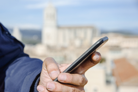 closeup of a young caucasian man using his smartphone in Girona, Spain, with the bell tower of the Cathedral in the backgroundの写真素材