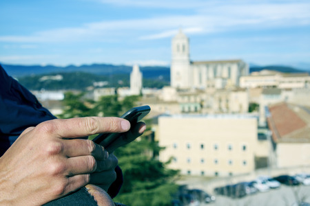 closeup of a young caucasian man using his smartphone in Girona, Spain, with the bell tower of the Cathedral in the backgroundの写真素材