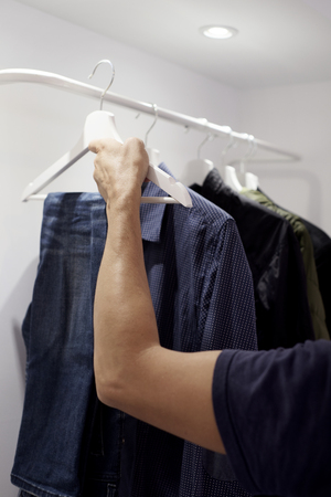 closeup of a young caucasian man hanging or unhanging a pair of jeans on the rack of a closetの写真素材