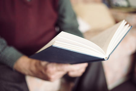 closeup of an old caucasian man reading a book sitting in a comfortable couchの写真素材