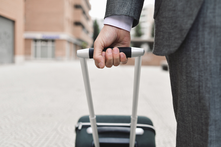 closeup of a young caucasian businessman in an elegant gray suit pulling a trolley by its handle on the streetの写真素材