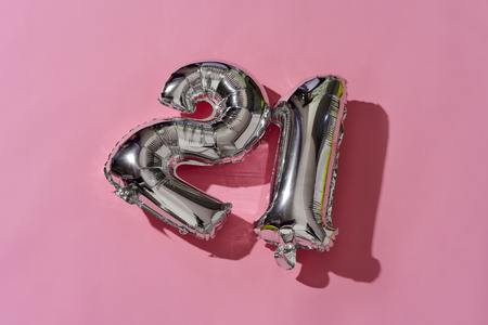 some silvery number-shaped balloons forming the number 21 against a pink background, with some blank space around themの写真素材