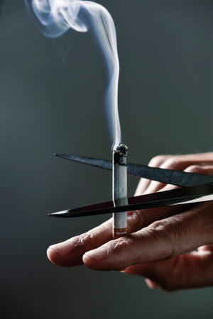closeup of a young caucasian man cutting a lit cigarette with scissors, depictign the idea of...