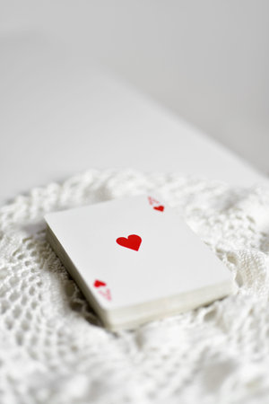 a deck of poker cards with the ace of hearts on top, on a crochet doily, placed on a white table,...