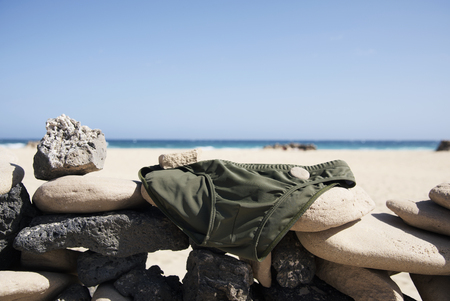 closeup of a green mens swuimsuit drying on a wall made with rocks on a beach in Fuerteventura, Canary Islands, Spainの写真素材