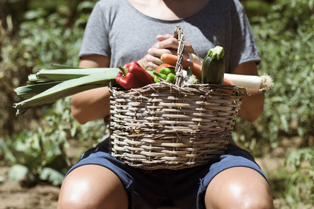 closeup of a young caucasian man with a rustic basket full of vegetables freshly collected in an organic orchardの写真素材
