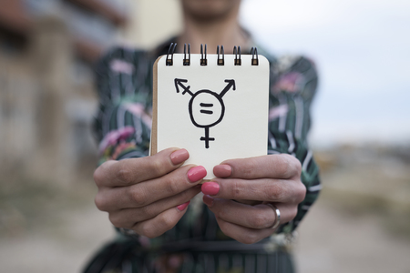 closeup of a young caucasian woman outdoors showing a notepad in front of her with a transgender symbol drawn in itの写真素材