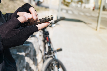 closeup of a young caucasian cyclist man wearing cycling gloves using his smartphone next to his bicycle outdoorsの写真素材