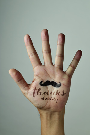 closeup of the palm of the hand of a young caucasian man with a mustache and the text thanks daddy written in it, against an off-white backgroundの写真素材