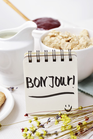 closeup of a table set for breakfast with a porcelain bowl with cereals, some toasts, a bowl with jam and a note with the text bon jour, good morning written in frenchの写真素材