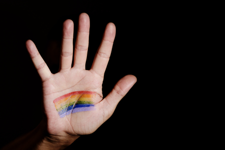 closeup of the hand of a young caucasian man with a rainbow flag painted in his palm, emerging from de darkness, and some blank space on the rightの写真素材
