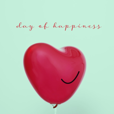 the text day of happiness and a red heart-shaped balloon with a smile drawn in it, against a pale green backgroundの写真素材