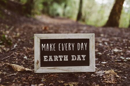 closeup of a wooden-framed chalkboard with the text make every day earth day written in it, on the ground in the woodsの写真素材