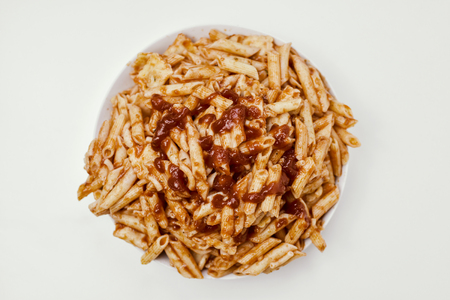 high angle view of a plate with an assortment of different cooked pasta served with tomato sauce on an off-white tableの写真素材