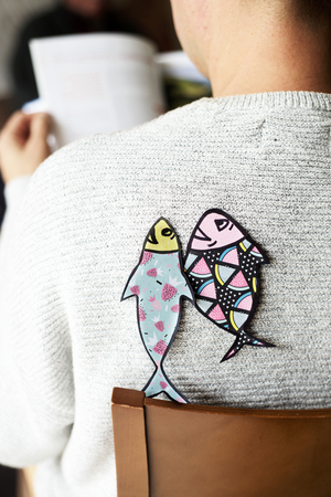 young caucasian man seen from behind with two paper fishes attached to his back, as a popular prank for april fools day in countries such as Italy, France, Belgium, Netherlands, Switzerland or Canadaの写真素材