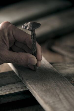 closeup of a young man driving a rusty nail on a wooden crossの写真素材