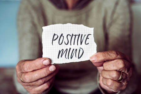 closeup of an old caucasian woman showing a note with the text positive mind written in itの写真素材