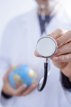 closeup of a young caucasian doctor man with a world globe in one hand and a stethoscope in the other handの写真素材
