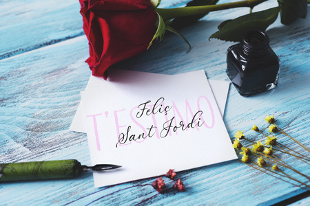 a red rose, an ink bottle, a nib pen and the text t estimo and Felic Sant Jordi, I love you and happy Saint George Day in Catalan, when it is tradition to give roses and books in Catalonia, Spainの写真素材