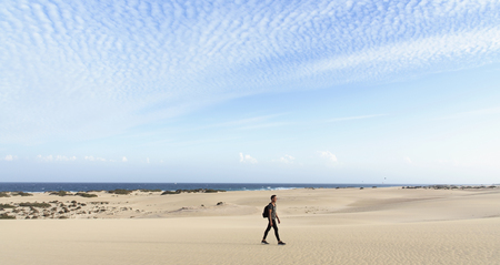 a young caucasian man, carrying a backpack, walking by the Corralejo dunes in Fuerteventura, Canary Islands, Spainの写真素材