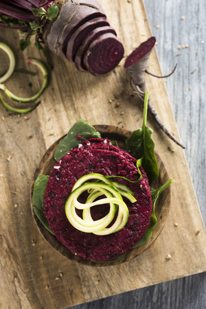 high angle view of some beet burgers on a wooden chopping board placed on a rustic wooden table, next to a sliced beetの写真素材
