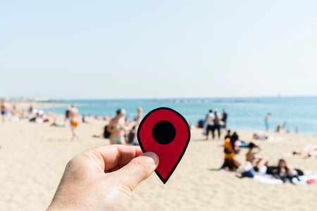 closeup of the hand of a young caucasian man with a red marker in La Barceloneta beach in Barcelona, Spain, with unrecognizable people sunbathing in the backgroundの写真素材