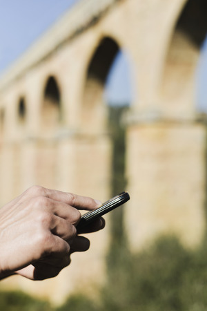 closeup of a young caucasian man with a smartphone in front of the roman aqueduct Pont del Diable in Tarragona, Spainの写真素材