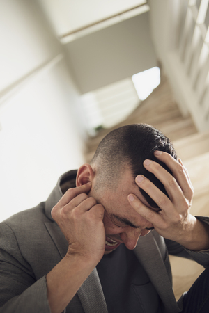 closeup of a suffering caucasian man with one hand in his head and the other hand covering his earの写真素材