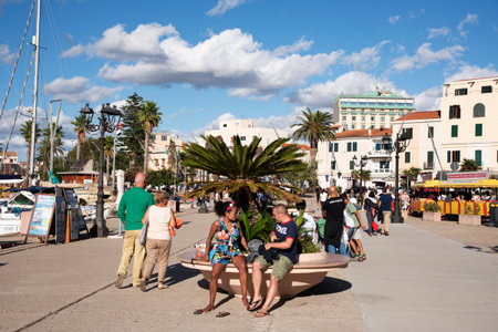 ALGHERO, ITALY -SEPTEMBER 17, 2017: People walking by the port of Alghero, Sardinia, Italy, next to...