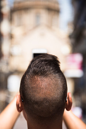 closeup of a young caucasian man seen from behind taking a picture of the Cathedral-Basilica of Our...