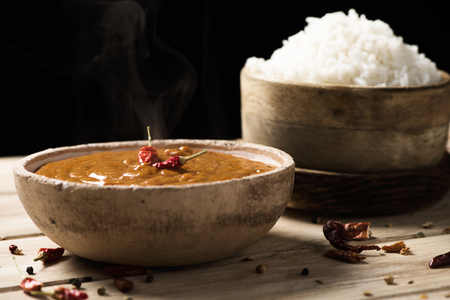 closeup of a bowl with a chicken korma curry and a bowl with cooked rice on an off-white wooden tableの写真素材