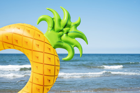 closeup of a swim ring in the shape of a pineapple on the beach, with the ocean and the blue sky in the backgroundの写真素材