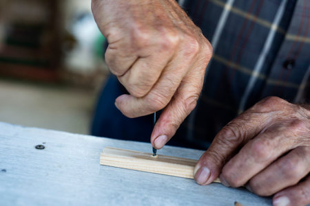closeup of an old caucasian man making a hole in a wood strip with a gimlet