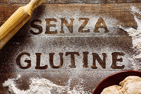 high angle view of a wooden table sprinkled with a gluten free flour where you can read the text senza glutine, gluten free in italian, next to a rolling pin and a piece of doughの写真素材