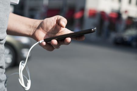 closeup of a young caucasian man outdoors using a smpartphone with a cable plugged into itの写真素材